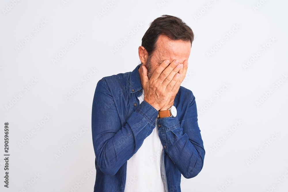 Middle age handsome man wearing blue denim shirt standing over isolated white background with sad expression covering face with hands while crying. Depression concept. Middle age handsome man wearing blue denim shirt standing over isolated white background with sad expression covering face with hands while crying. Depression concept.
