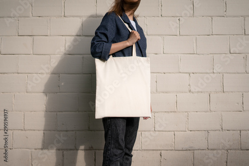 Urban mockup of tote bag. Girl holding white cotton tote bag on a brick wall background. Template can be used for you design 