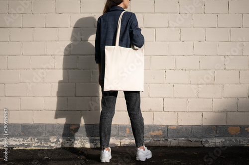 Urban mockup of tote bag. Girl holding white cotton tote bag on a brick wall background. Template can be used for you design 
