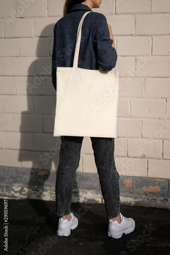 Urban mockup of tote bag. Girl holding white cotton tote bag on a brick wall background. Template can be used for you design 