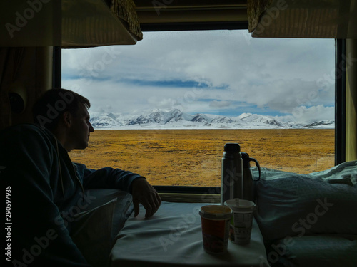 CLOSE UP: Male traveler looks at mountains through the window of overnight train