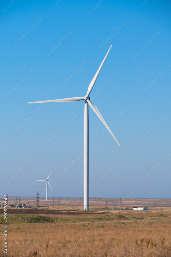 Huge wind generators against blue sky, close up. Spinning wind turbines on blue sky background, close up Huge wind generators against blue sky, close up. Spinning wind turbines on blue sky background, close up