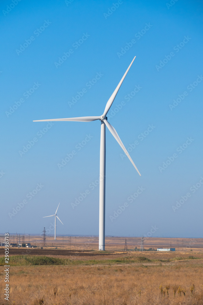 Huge wind generators against blue sky. Group of spinning wind turbines in wheat field on blue sky background Huge wind generators against blue sky. Group of spinning wind turbines in wheat field on blue sky background