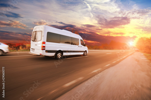 A van and other cars driving fast on the countryside road against a sky with a sunset
