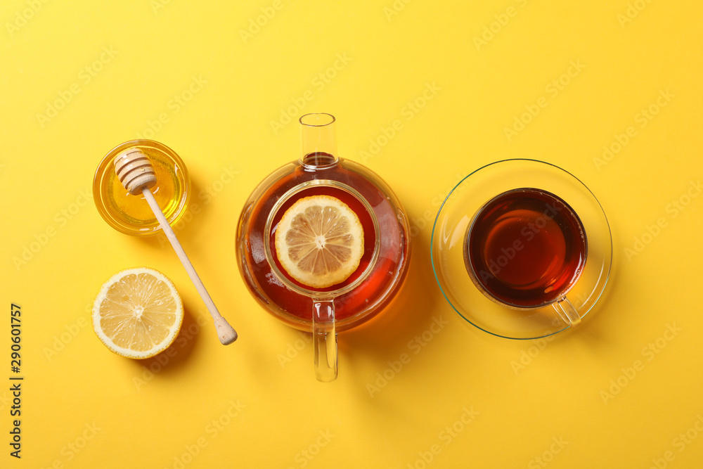 Flat lay. Cup of tea, teapot, lemon, honey and dipper on yellow background, copy space