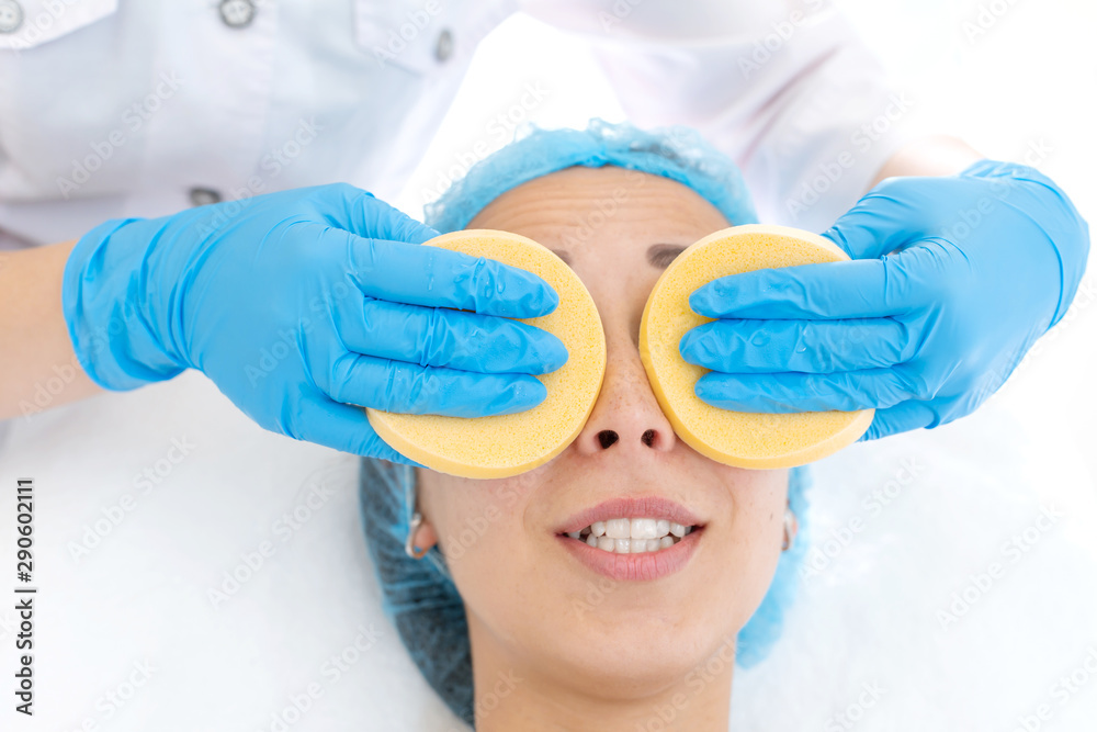 Fototapeta premium close-up hands of beautician makes client facial massage sponges