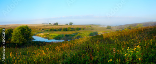 Hazy summer morning landscape with small river and fields