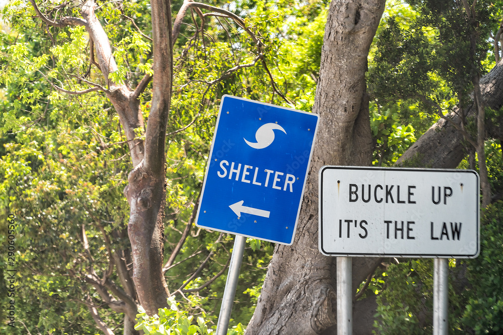 Hurricane evacuation shelter blue sign on road and seat belt buckle up it's the law text with arrow direction in Naples, Florida coast during day