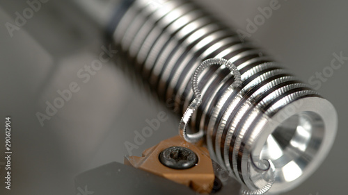 MACRO: CNC machine slowly threading a small metal workpiece into a shiny screw