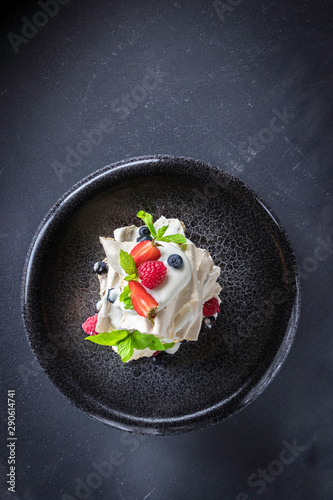Dessert Pavlova with strawberry, raspberry, mint, bilberry on a grey plate and background. Top view