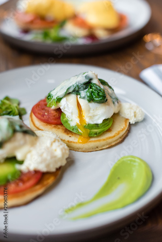 Pancakes with poached egg, tomato, avocado and sauteed spinach. Close up view.