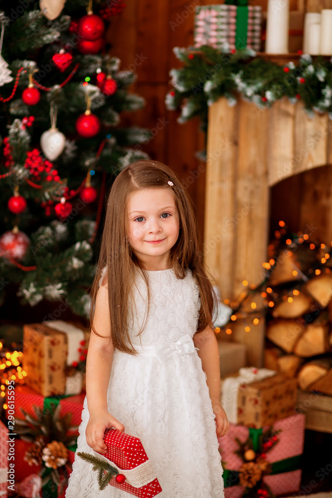 happy cute girl of 4-5 years old in an elegant white dress by the fireplace near the Christmas tree