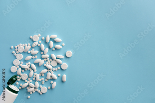Bottle with scattered pills on blue background. Flat lay.