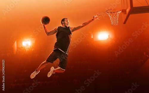 African american professional basketball player on basketball court in action with the ball. Slam Dunk. Red floodlit background © TandemBranding