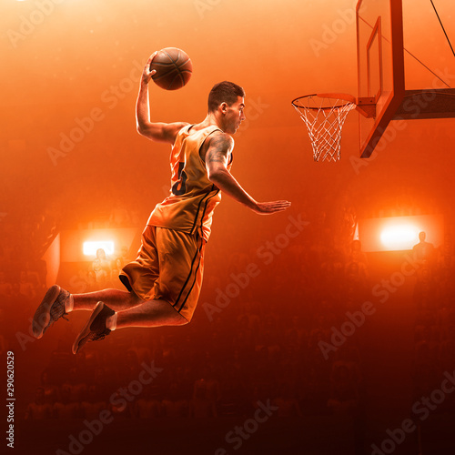 Professional basketball player on basketball court in action with the ball. Slam Dunk. Red floodlit background