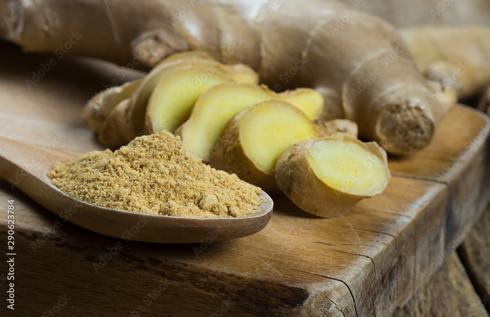 Fototapeta premium Fresh chopped ginger root and ground ginger powder in wooden spoon on wooden rustic table. Healthy food spice concept. Zingiber officinale