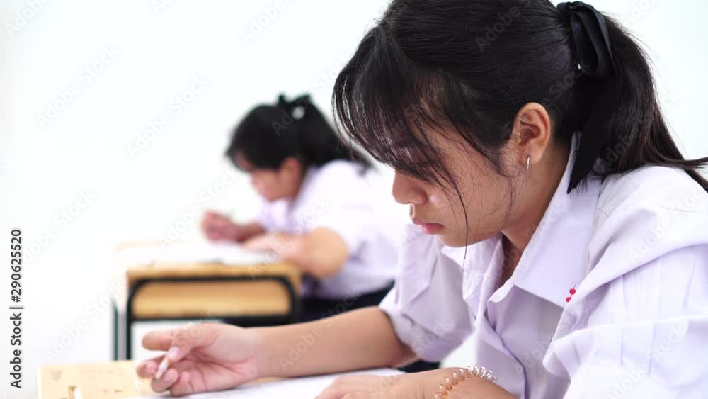 Test in high school /university student in exam room concept, Asian students group holding pencil writing paper answer sheet and sitting on taking final examination in classroom with Thai uniform Test in high school /university student in exam room concept, Asian students group holding pencil writing paper answer sheet and sitting on taking final examination in classroom with Thai uniform