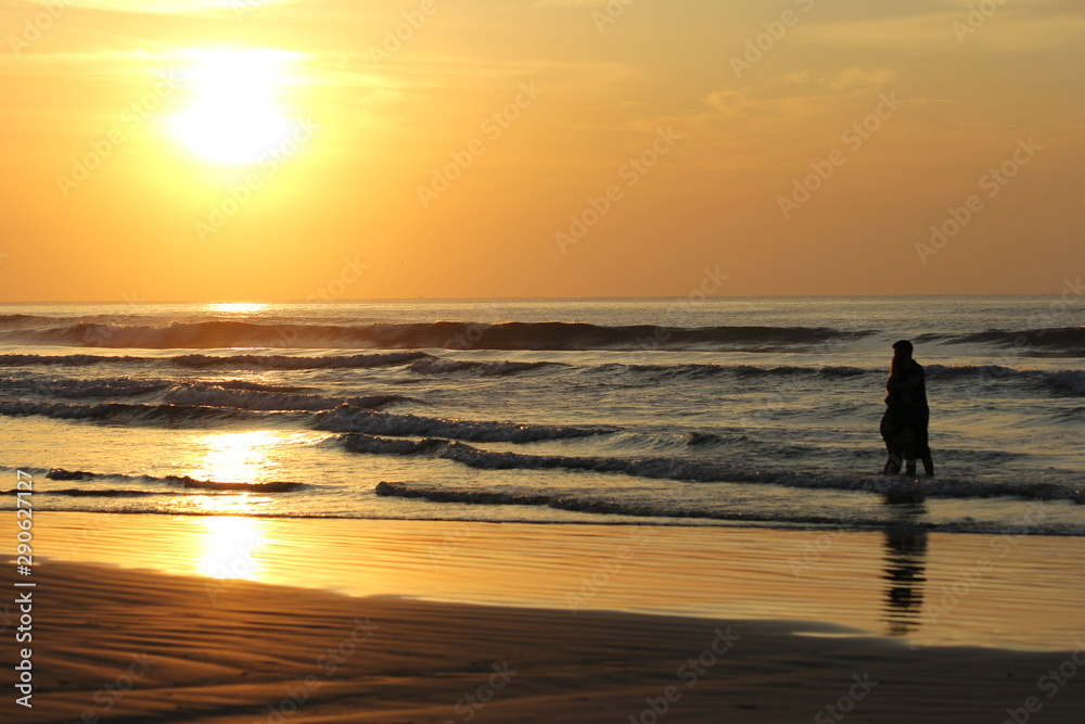 Silhouette of a couple embraced on the waters of a beach. Sunset with orange sky and reflections in the water.