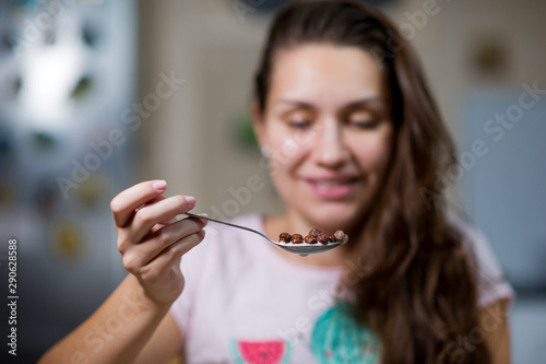 The girl holds in the air a spoon with chocolate flakes and milk  about to eat them. front view