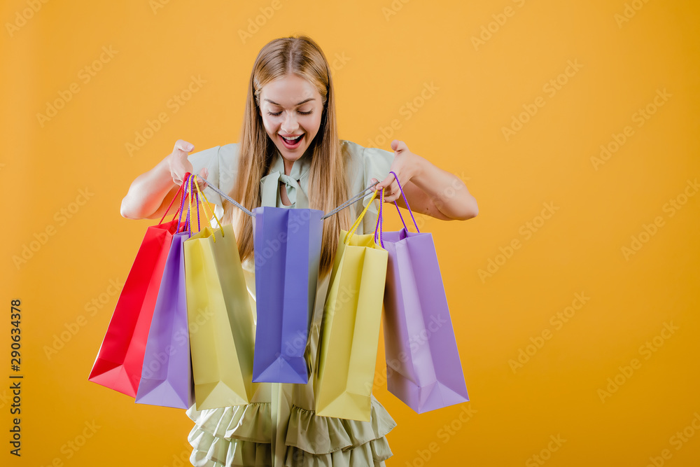 surprised young beautiful girl with colorful shopping bags isolated over yellow