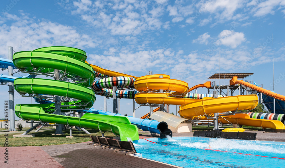 Water park, bright multi-colored slides with a pool. A water park without people on a summer day with a beautiful, cloudy blue sky