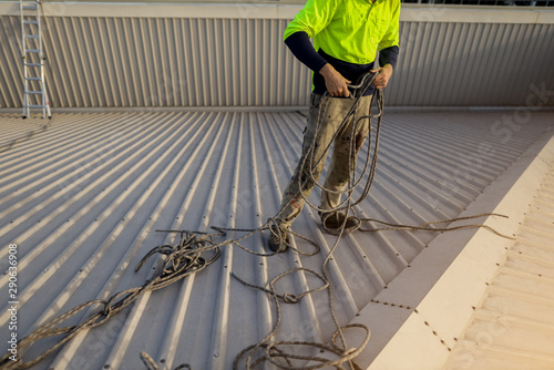 Wide angle pic of rope access construction worker standing on top of the roof conducting safety inspecting uncoiling twisting rope prior used construction site Sydney, Australia