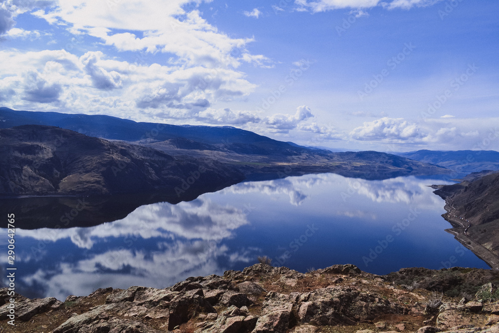 View of kamloops lake from Battle Bluff hike, clouds and mountains are reflecting in the calm lake, rocks