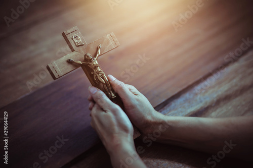 Obraz na plátně Close up of woman hands holding crucifix of Jesus Christ while praying to God on wooden table background, Christian trust and faith concept with copy space