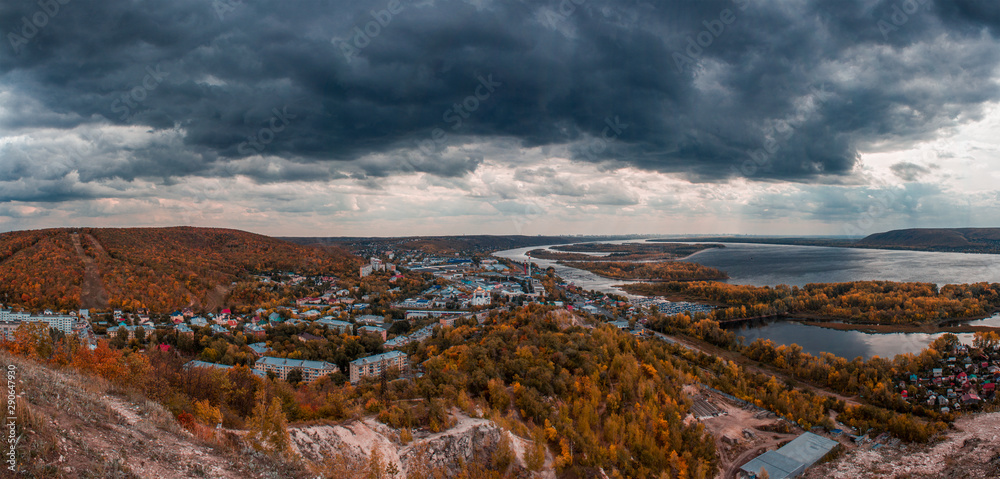 Obraz Black clouds over the city. Panoramic view from the mountains to the orange autumn landscape of the city, forests and rivers with islands. Red clay, the Volga river in the city of Samara.