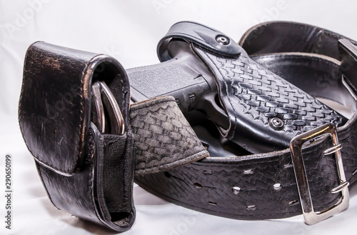 A worn police duty belt with a black pistol and handcuff case wrapped up on a white background photo