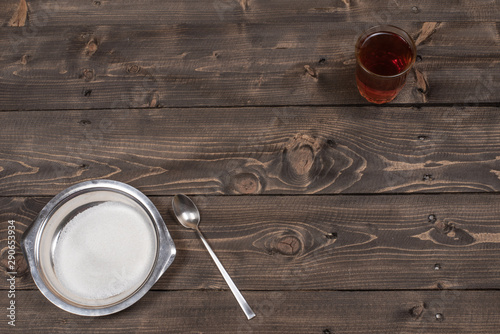 Tea in a glass, teaspoon and sugar in a stainless plate on a wooden vintage table top view, flat lay