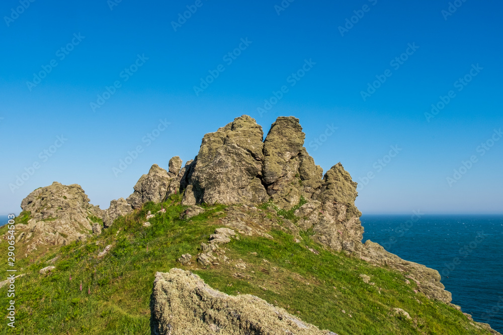Rock formations protruding out of a green and grass hillside that overlooks the sea near Start Point Lighthouse on a clear day in England, UK. Rock formations protruding out of a green and grass hillside that overlooks the sea near Start Point Lighthouse on a clear day in England, UK.