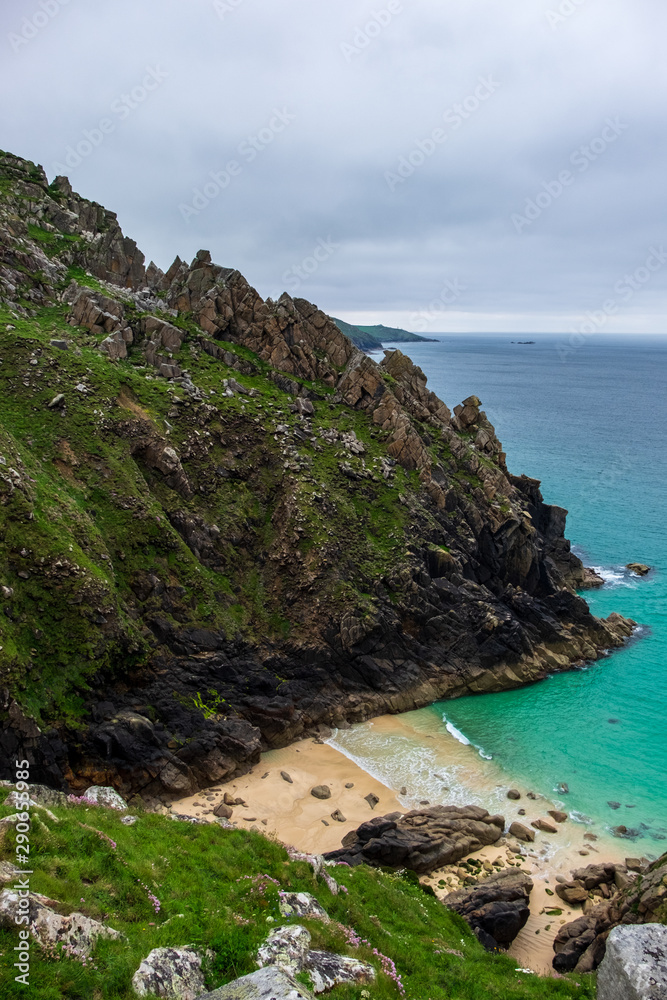 A new yellow and sandy beach is revealed underneath the green and rocky cliffs on this cloudy day in England, UK.