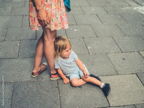 Sad crying toddler sitting in the street by his mother's feet