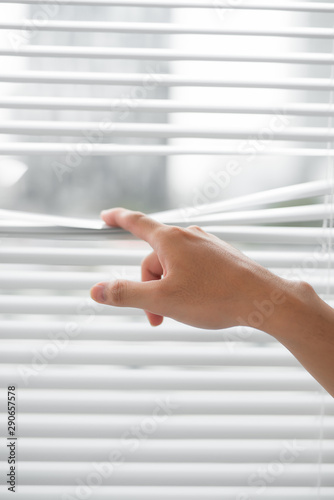 It's a sunny day outside. Man's hand taking a peak through the window blinds.