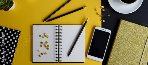 Flat lay office table desk in midern design in yellow and black color with office supplies, dotted notebook , smartphone and pencil. Panoramic top view. photo