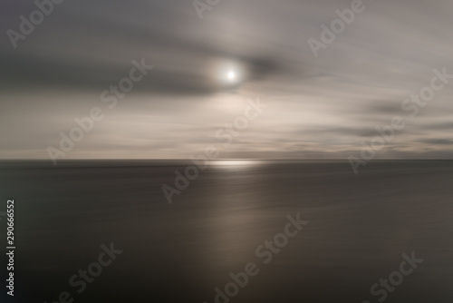 A long exposure has made the sea look like silver as the sun above sit stick with the clouds streaking across the sky.