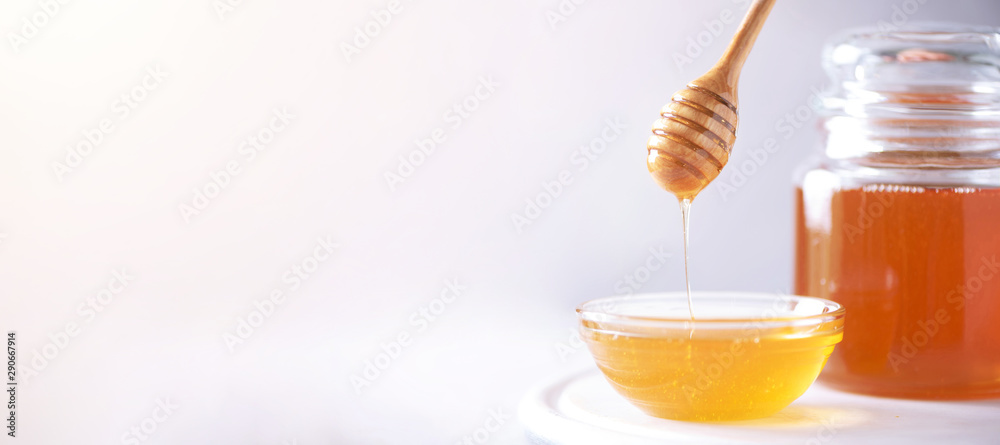 Honey dripping from wooden honey spoon in jar on grey background. Copy space. Autumn harvest concept. Banner Honey dripping from wooden honey spoon in jar on grey background. Copy space. Autumn harvest concept. Banner