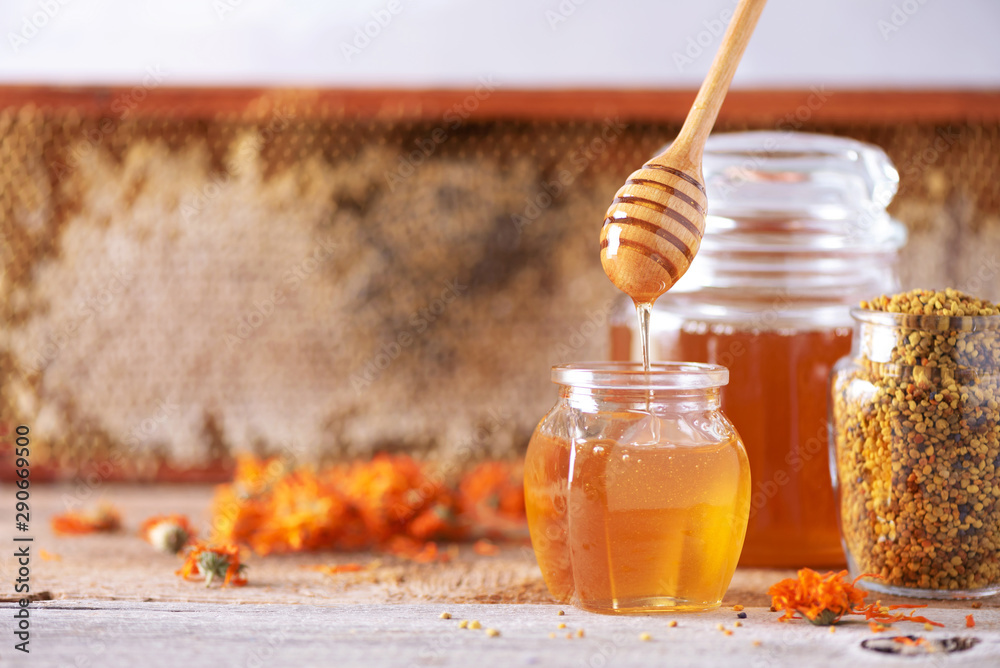 Herbal honey in jar with dipper, honeycomb, bee pollen granules, calendula flowers on grey background. Herbal honey in jar with dipper, honeycomb, bee pollen granules, calendula flowers on grey background.