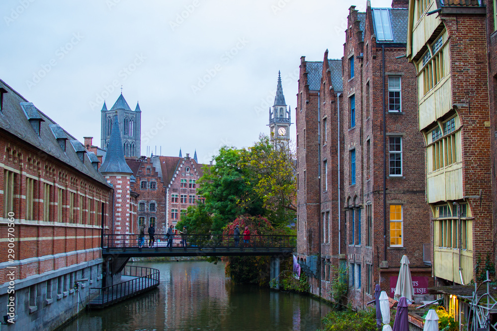Obraz premium Ghent, Belgium; 10/28/2018: Typical colorful belgian houses near Lys river (Leie) with the Belfry and the tower of St Nicholas' Church at the background