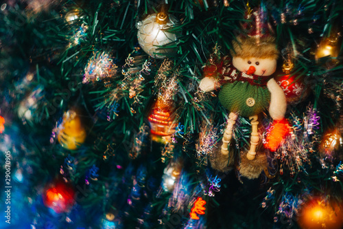 A Christmas toy in the form of a snowman hangs on an artificial Christmas tree with colorful bright lights. Long exposure photo. © Svyatoslav Balan