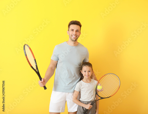 Little girl and her father with tennis rackets on color background photo