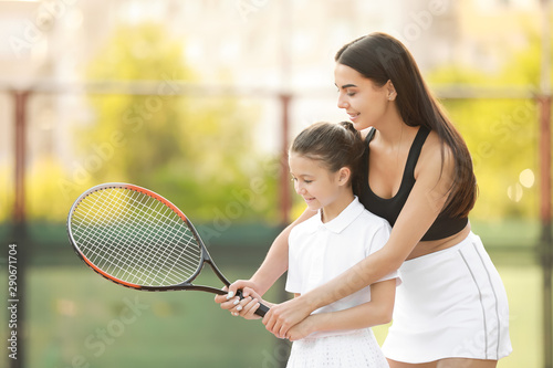 Little girl and her mother playing tennis on court