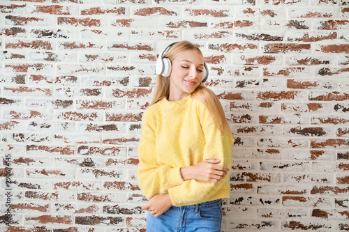 Beautiful young woman listening to music against brick wall