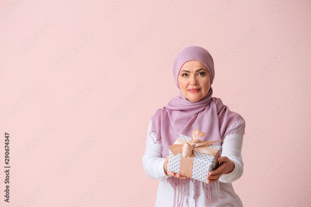 Beautiful mature Muslim woman with gift box on color background Beautiful mature Muslim woman with gift box on color background