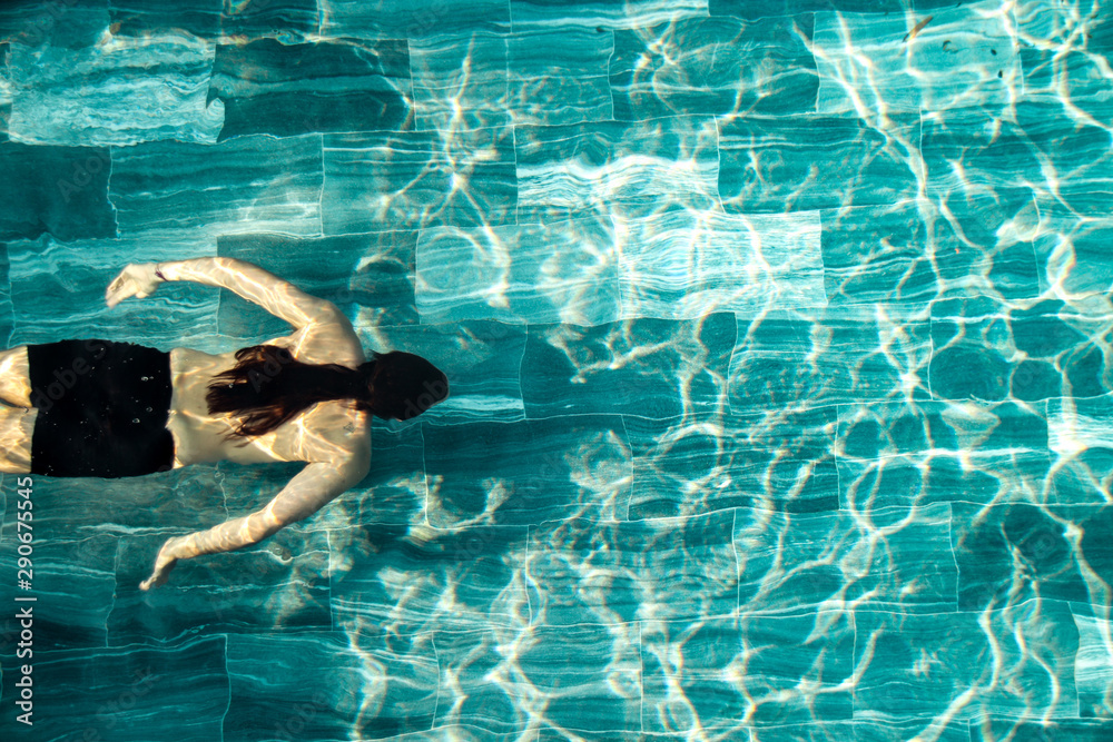Top view of a long haired man swimming laps on a pool