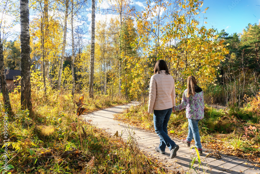 Fototapeta premium Mother and little girl walking together on the wooden walkway on a sunny autumn day.
