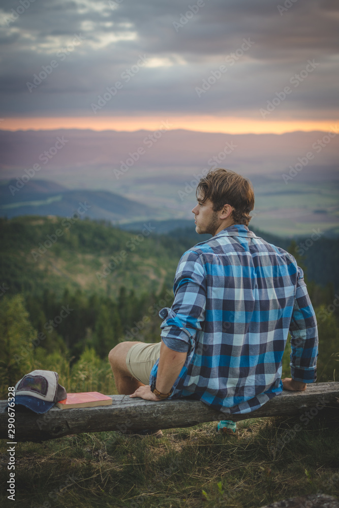 Young handsome Caucasian man relaxing while hiking on top of the mountain