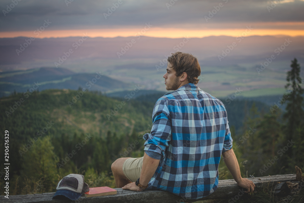 Young handsome Caucasian man relaxing while hiking on top of the mountain