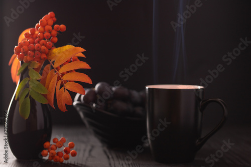 Cup of tea, a twig of rowan-tree in a vase and black grapes, selective focus.